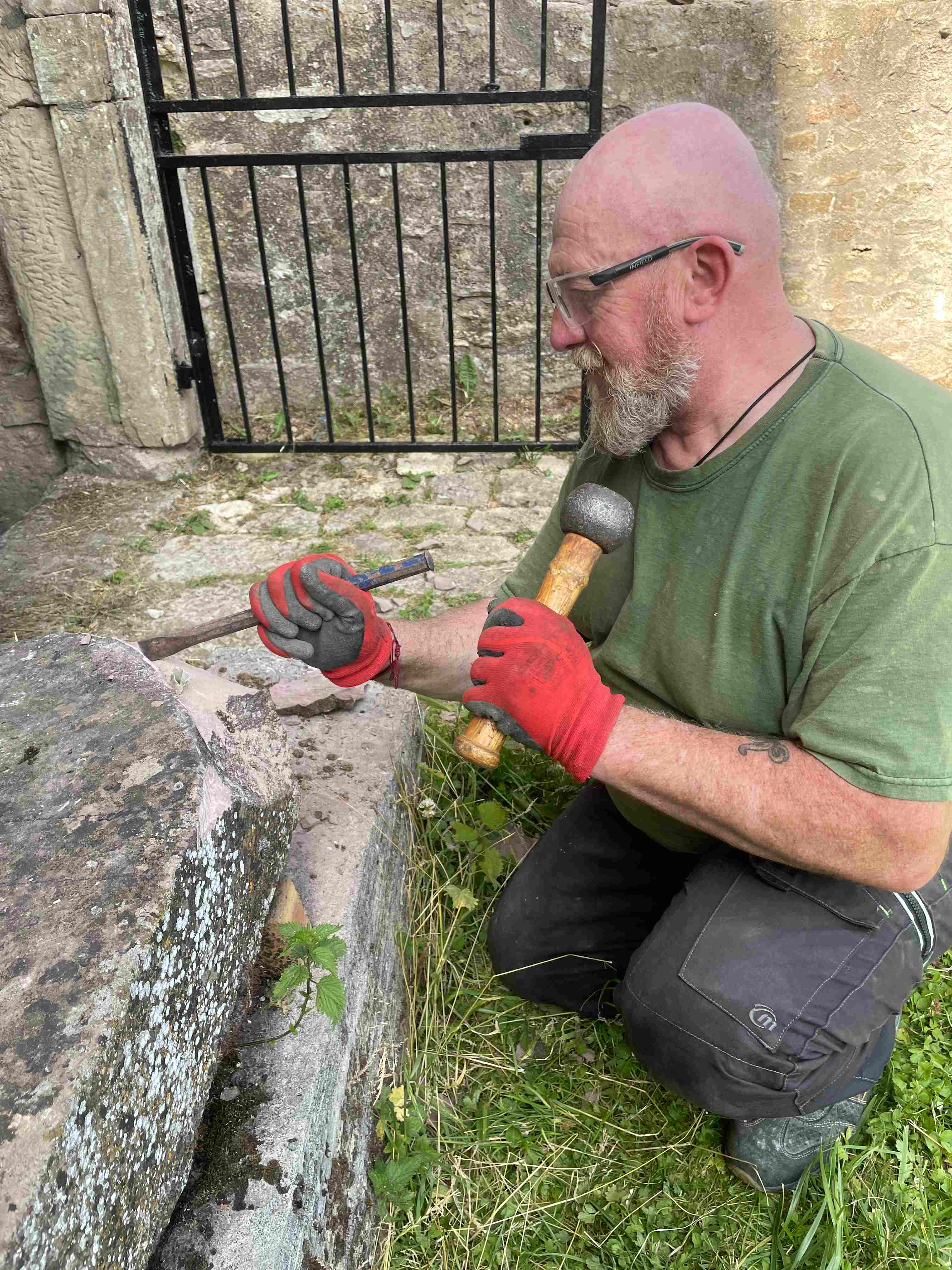Un artisan taille une pierre au maillet près des remparts